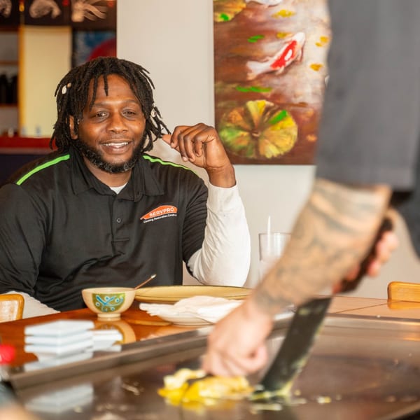 A man smiling at a hibachi chef cooking on a grill at Shiki Japanese Thai Sushi Bar.