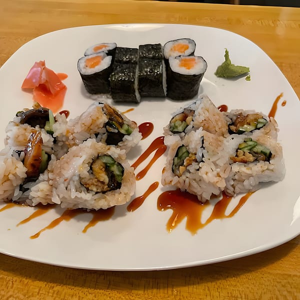 A white plate of sushi rolls, including salmon maki and eel rolls with sauce, ginger, and wasabi.