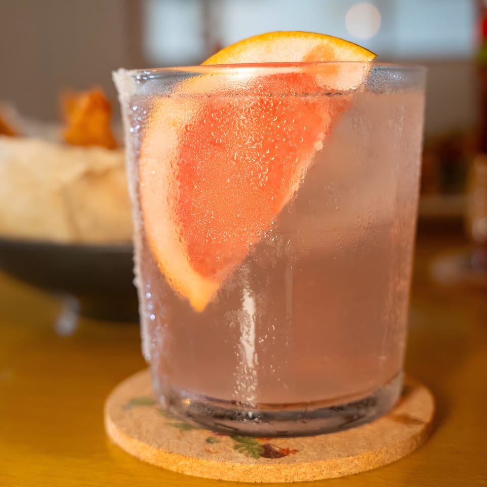A refreshing Shiki Japanese Thai Sushi Bar cocktail with a grapefruit slice, condensation, and a salt rim.