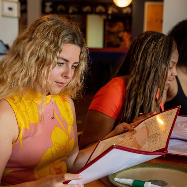 Two women at Shiki Japanese Thai Sushi Bar looking at menus, one in a pink and yellow top.