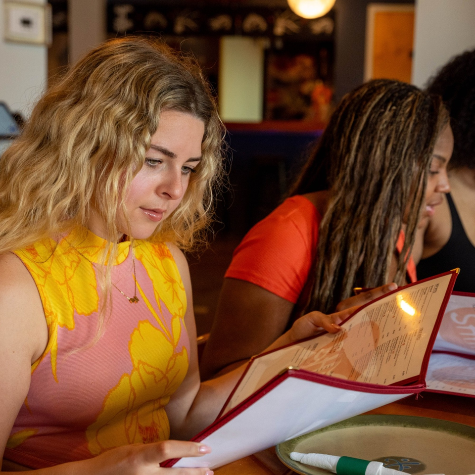 Two women at Shiki Japanese Thai Sushi Bar looking at menus, one in a pink and yellow top.