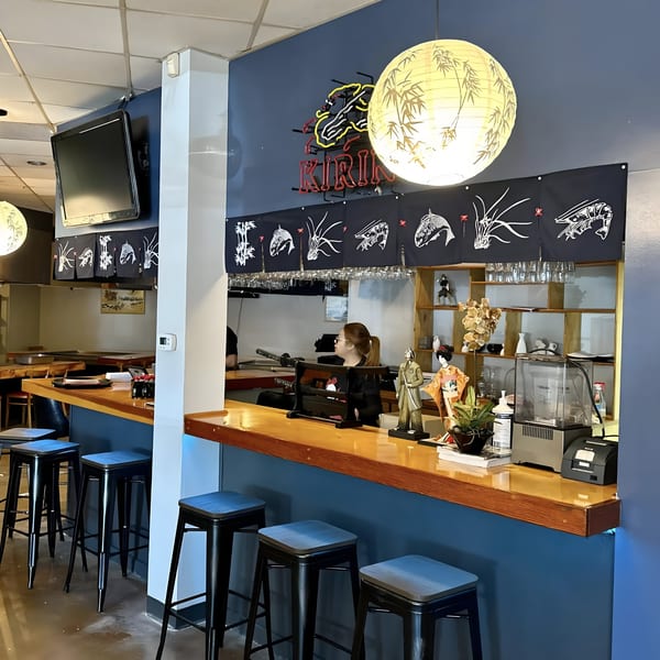 Interior of Shiki Japanese Thai Sushi Bar with a bar, stools, and a neon Kirin sign.