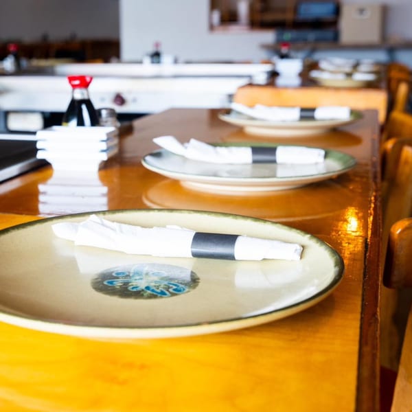 Place settings with plates, rolled napkins, and soy sauce bottles on a wooden table at Shiki Japanese Thai Sushi Bar.
