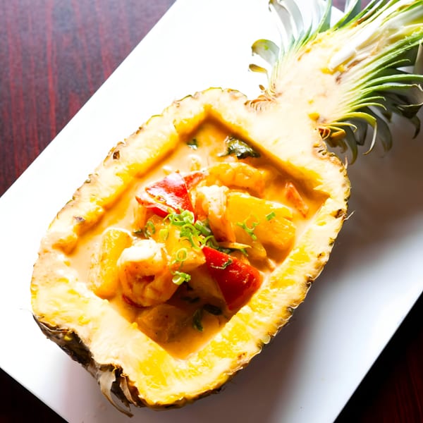 Pineapple curry with shrimp, red peppers, and green onions served in a hollowed-out pineapple.