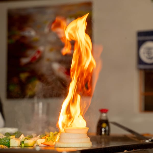 A hibachi chef creates an onion volcano with a large flame on a Shiki Japanese Thai Sushi Bar grill.